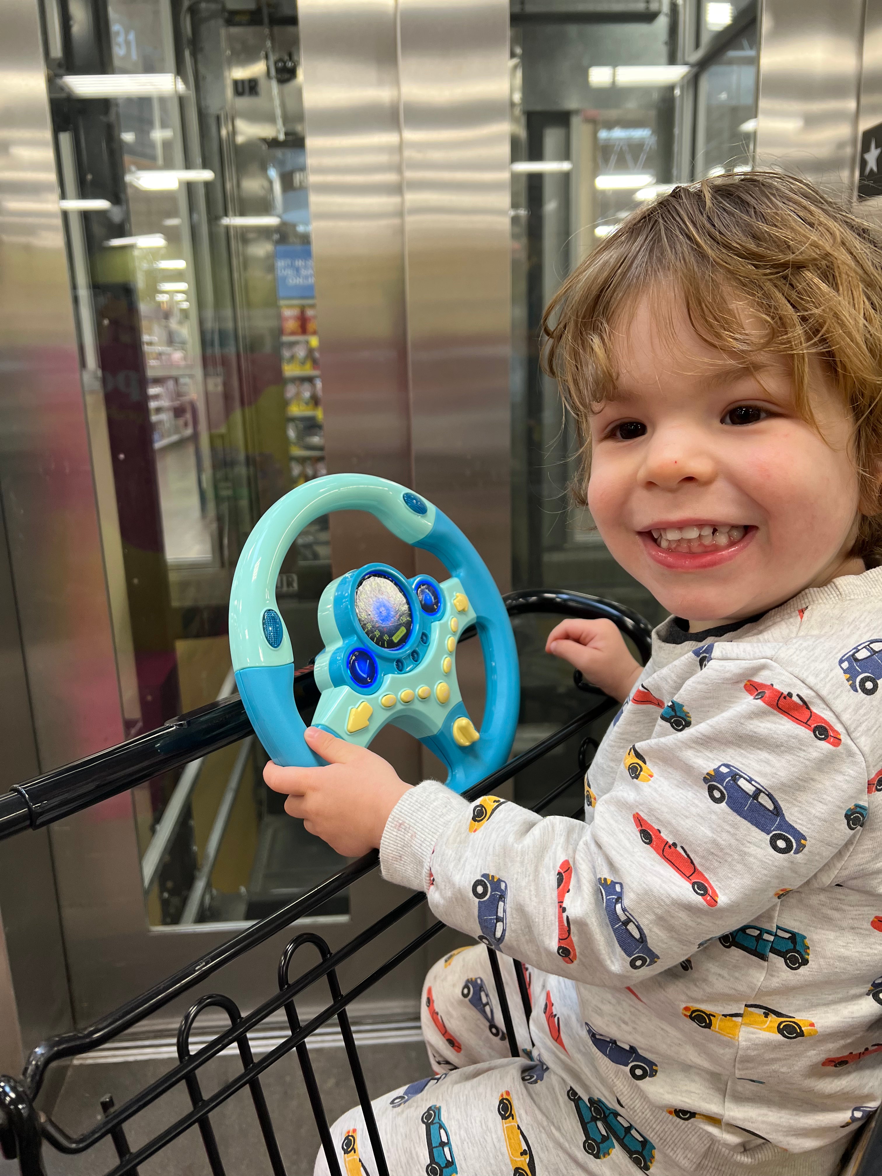 Child in a shopping cart with steering wheel attachable toy